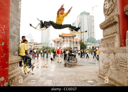 Young adult doing splits on jumping stilts, Kunming, Yunnan , China Stock Photo