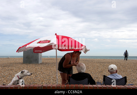 people under a beach umbrella on Brighton shingle beach Stock Photo