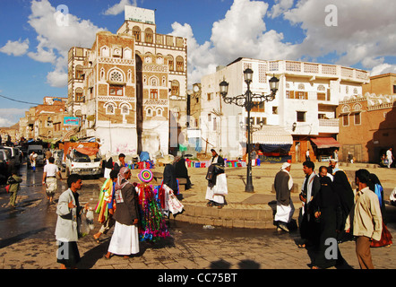 Yemen, Sanaa, busy market street with hawker holding articles for sale, group of people walking on street Stock Photo