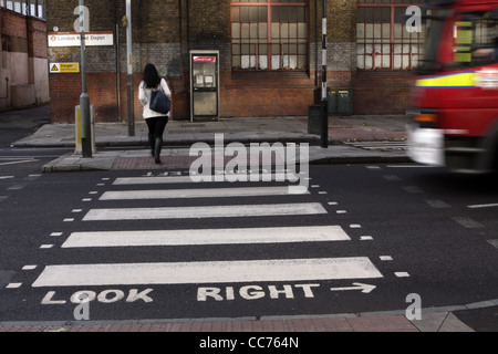 a female walks across a zebra crossing in London while a vehicle accelerates behind her Stock Photo