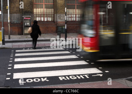 a female walks across a zebra crossing in London while a bus accelerates behind her Stock Photo