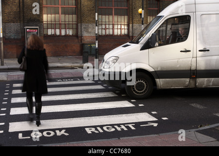 a female walks across a zebra crossing in London while a van waits Stock Photo