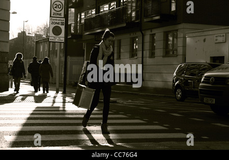 a female walks across a zebra crossing in London while a vehicle waits and people walk in the background, photographed in sepia Stock Photo