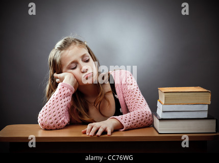 Unhappy caucasian schoolgirl at her desk, near a stack of books Stock Photo