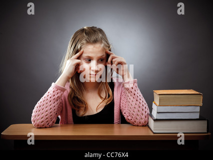 Unhappy caucasian schoolgirl at her desk, near a stack of books Stock Photo