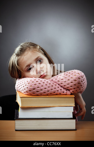 Unhappy caucasian schoolgirl at her desk, near a stack of books Stock Photo