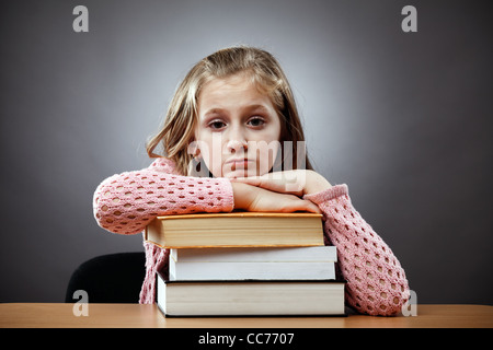 Unhappy caucasian schoolgirl at her desk, near a stack of books Stock Photo