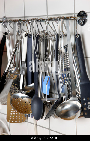 Various kitchen utensils, kitchen tools, hanging at a kitchen wall rack. Stock Photo