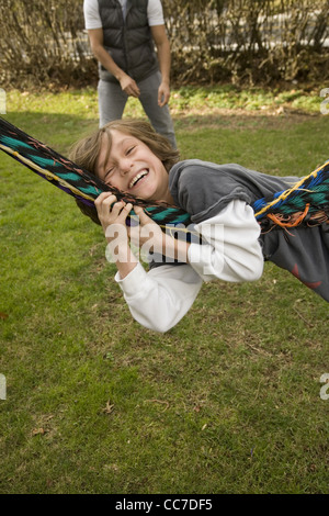 Seven year old boy being swung on the family hammock by dad in the background. Stock Photo