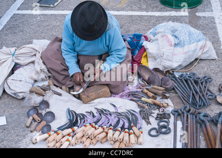 An older Andean Indian woman sits on the ground selling saws and other metal objects in the outdoor marker in Saquisili, Ecuador Stock Photo