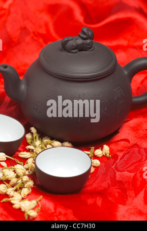 jasmine tea dry flowers,pot and two cups ,over red silk tablecloth Stock Photo