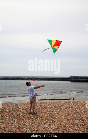 A lone kite flier struggles to get his kite airborne on the beach at Lyme Regis, Dorset, England, UK Stock Photo