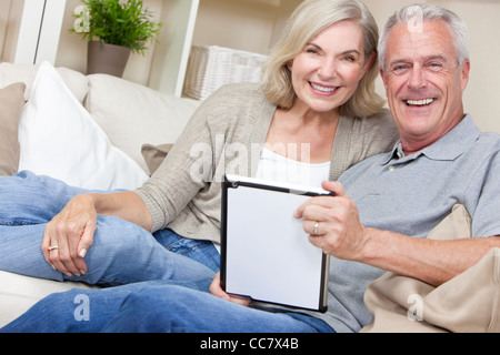 Happy senior man and woman couple sitting together at home smiling and happy using a tablet computer Stock Photo