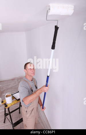 Decorator using a roller extension to paint a ceiling white Stock Photo