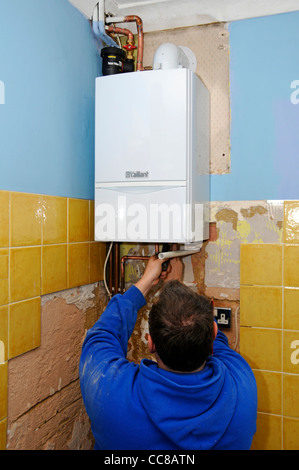 Condensing gas boiler being installed by plumber man to replace failed old unit (see 17�Թ����� Additional info panel) part of kitchen home improvement UK Stock Photo