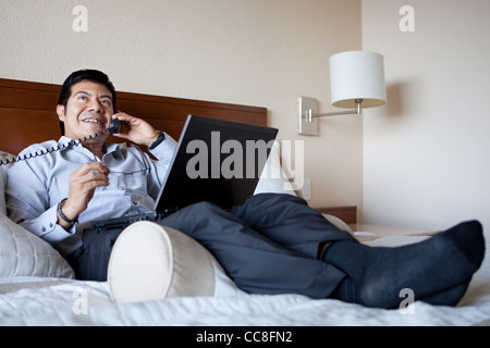 Hispanic businessman on the phone and using laptop in his hotel room Stock Photo