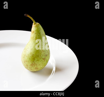 Ripe juicy pear on white plate with black background Stock Photo