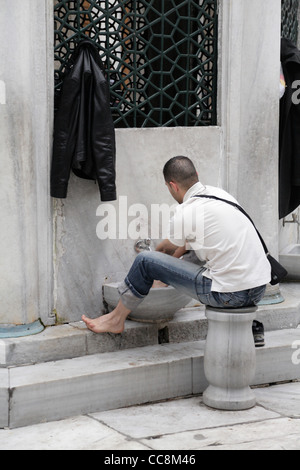 Young muslim man washing his feet at mosque wudu The New Mosque Yeni Cami. Ritual washing prior to prayer islam islamic law Stock Photo