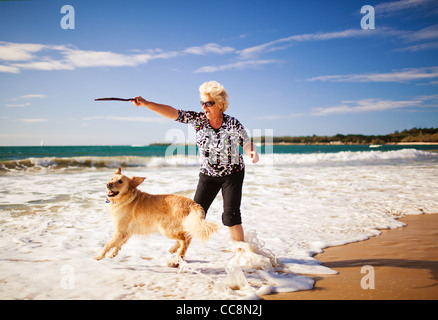 Happy woman playing on the beach with golden retriever Stock Photo