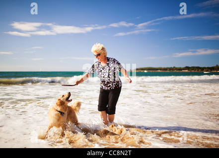 Happy woman playing on the beach with golden retriever Stock Photo