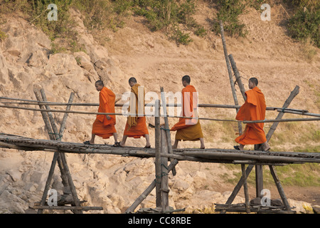 Young Buddhist monks walking across a bamboo bridge in Luang Prabang, Laos Stock Photo