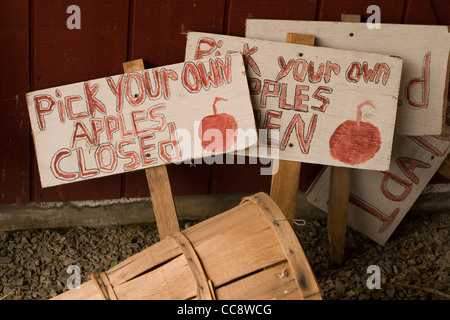 A basket lays on its side with a stack of signs for a pick-your-own apple orchard. Stock Photo