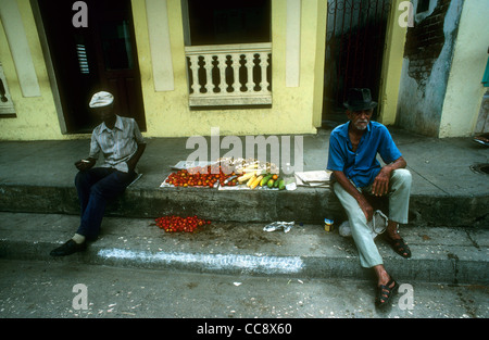 Two men sitting beside the road selling home-grown vegetables in the small east Cuban town of Baracoa Stock Photo