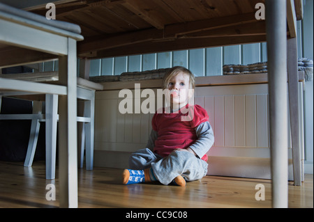 Young Girl Sitting on Floor Underneath Table, Sweden Stock Photo