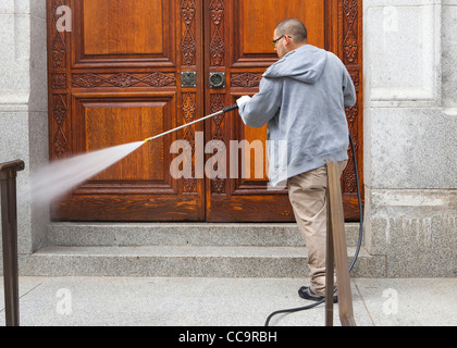 A maintenance man cleaning entrance of building using a pressure washer Stock Photo
