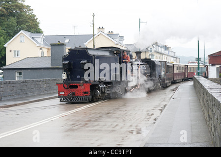 A steam locomotive with a passenger train on the Welsh Highland Line crossing the road at Porthmadog Stock Photo