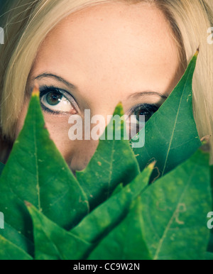 Close-up portrait of a beautiful girl holding leaves in front of face
