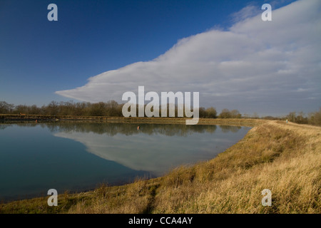 The sharp edge of a cloud bank is reflected in the perfectly still blue water of a reservoir Stock Photo