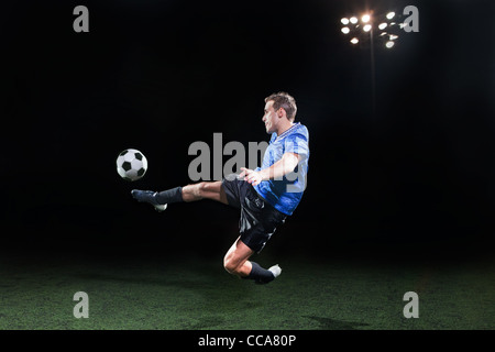 Young soccer player leaping into air to kick ball Stock Photo