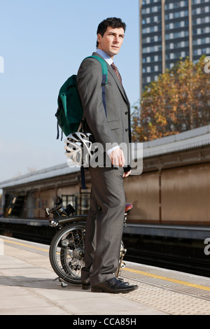 Mid adult businessman carrying folding bicycle on railway platform Stock Photo
