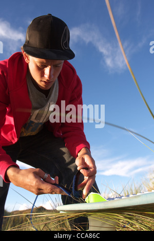 A surfer prepares his surf board ready for a surf in the sand dunes. Stock Photo