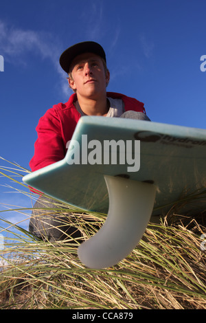 A surfer prepares his surf board ready for a surf in the sand dunes. Stock Photo