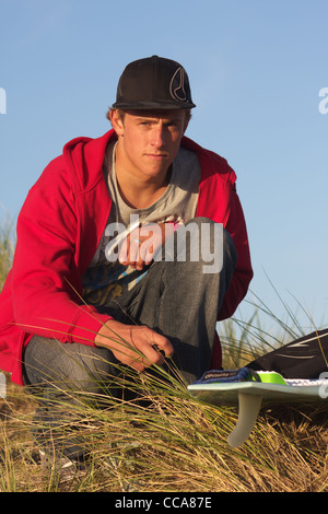 A surfer prepares his surf board ready for a surf in the sand dunes. Stock Photo