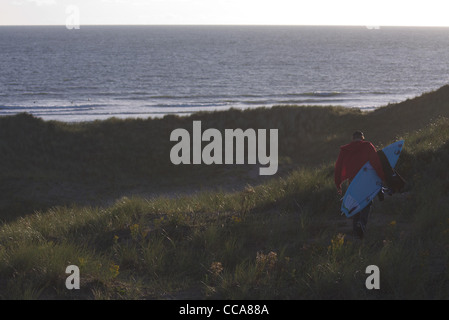 A surfer makes his way over sand dunes towards the beach in the late summer sun. Stock Photo