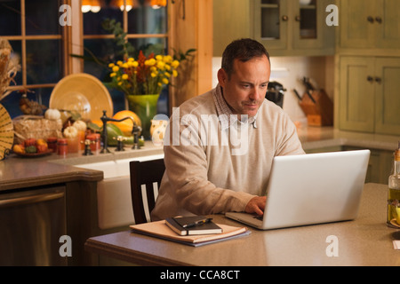Mature man working on laptop in kitchen Stock Photo