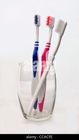 three toothbrushes in a glass, pink blue and white. Stock Photo