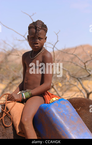 Young Himba girl on a donkey fetching water. Kaokoland, Northern Namibia. Stock Photo