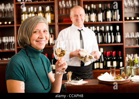 Wine bar senior woman enjoy wine glass in front of bartender Stock Photo