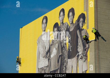 Abseiling workers fixing giant photographic image of an Indian family on the Southbank, London, England Stock Photo