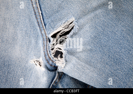 Close up of hole in an old pair of blue jeans showing the frayed threads. Stock Photo