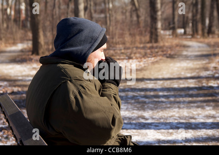 Homeless man on park bench trying to keep hands warm on cold winter day. Stock Photo