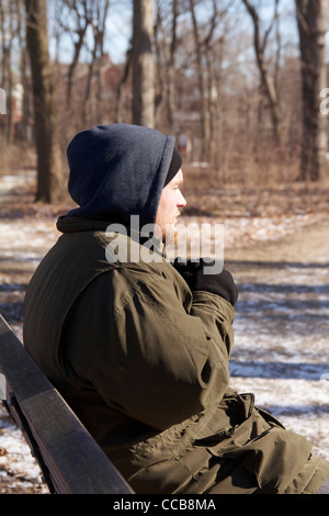 Homeless man on park bench on cold winter day. Stock Photo