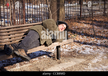 Homeless man sleeping on park bench on cold winter day. Stock Photo