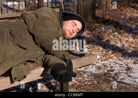 Homeless man sleeping on park bench on cold winter day. Stock Photo