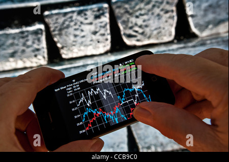 SILVER PRICE TRADING BUYING Hands holding Apple iPhone smartphone displaying live on-screen silver bid prices, pure silver bullion bars in background Stock Photo