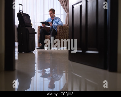 Mid adult caucasian manager typing on tablet pc in hotel room during business travel. Low angle view, full length Stock Photo